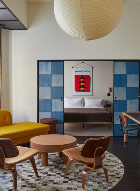 A large living space with a stylish yellow sofa and large traditional light fixture opens onto a dedicated bedroom