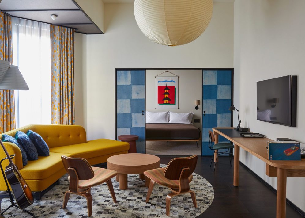 A large living space with a stylish yellow sofa and large traditional light fixture opens onto a dedicated bedroom