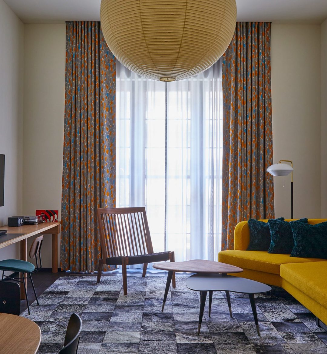 A large living space with a stylish yellow sofa and large traditional light fixture features a window providing natural light to the entire room