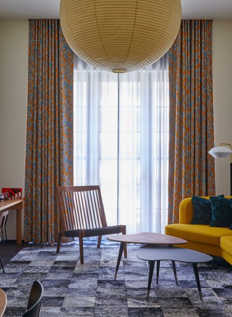 A large living space with a stylish yellow sofa and large traditional light fixture features a window providing natural light to the entire room