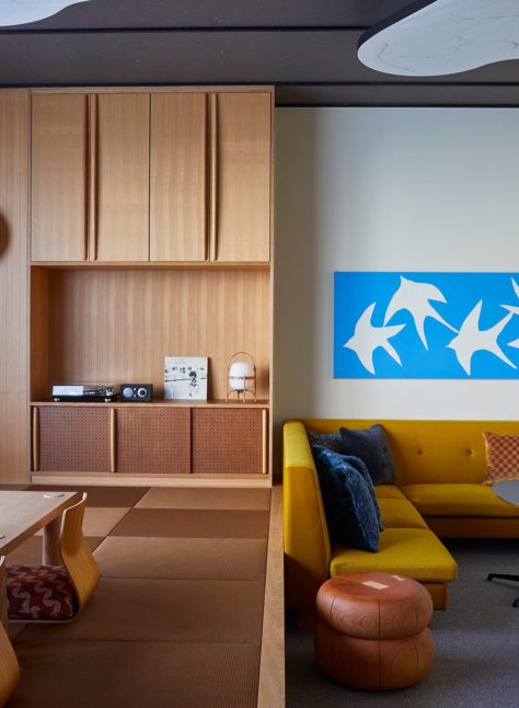 A spacious room is separated into two parts – one area features a stylish yellow couch and more seating, and the other area provides a table close to the floor for tea