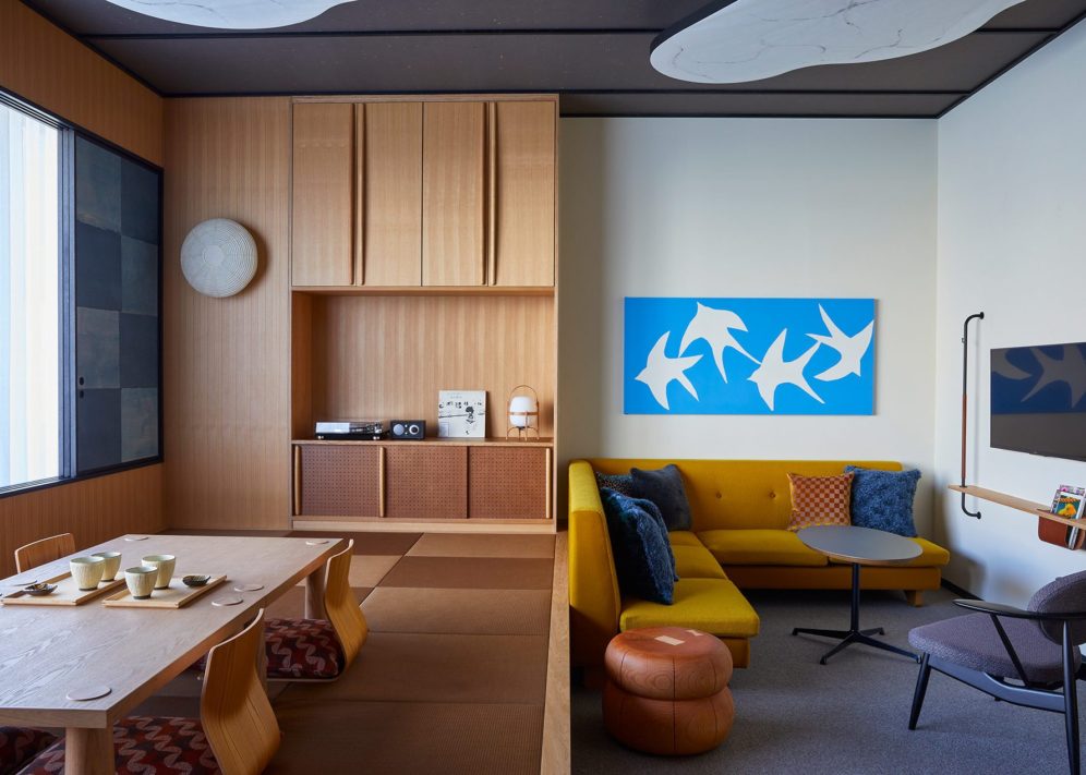 A spacious room is separated into two parts – one area features a stylish yellow couch and more seating, and the other area provides a table close to the floor for tea