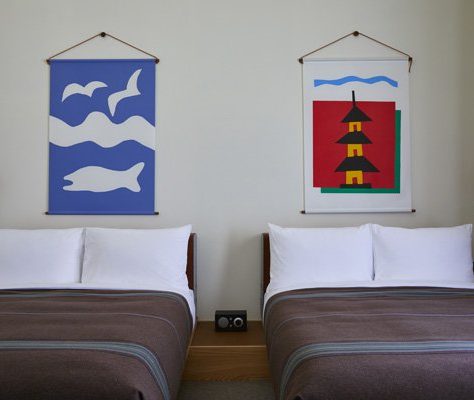 Two beds with brown bedding are flanked by stylish wall mounted lamps, and a radio sits between therm